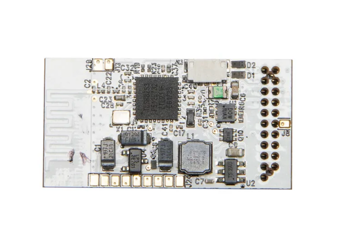 A white electronic circuit board with various electronic components, a central black integrated circuit chip, and a row of gold-plated pins on the right side, photographed on a solid white background.