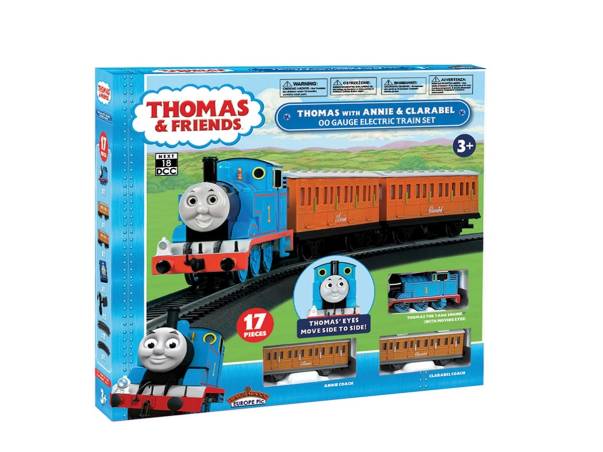 Thomas with Annie & Clarabel OO Gauge Electric Train Set in its retail packaging, featuring a blue steam locomotive and orange passenger carriages on a green illustrated track background.