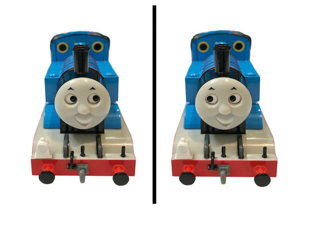 Two toy model trains resembling Thomas the Tank Engine, shown side by side on a plain white background, with a vertical black divider between them.